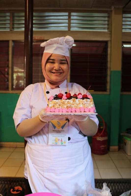 Siswa berseragam koki memegang kue buatannya