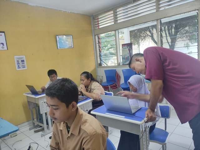 Guru mendampingi siswa belajar TIK